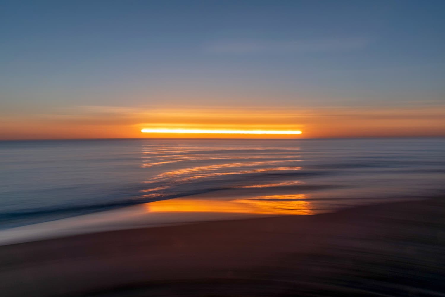 First light over open water, the sun a single line on the horizon.